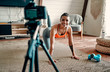 © Valerii Apetroaiei - Athletic woman blogger in sportswear shoots video on camera as she does exercises at home in the living room. Sport and recreation concept. Healthy lifestyle.