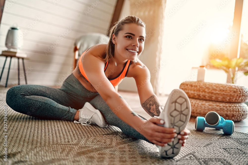 Athletic woman in sportswear doing fitness stretching exercises at home in the living room. Sport and recreation concept. - obrazy, fototapety, plakaty 