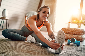 Athletic woman in sportswear doing fitness stretching exercises at home in the living room. Sport and recreation concept.