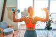 © Valerii Apetroaiei - Determined woman losing weight at home and exercising with dumbbells. Sport and recreation concept. Beautiful woman in sportswear with blue dumbbells in her hands.