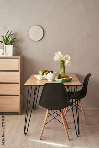 Loft style dining room. Dining table with chairs. Mock up interior photo. Black chairs at dining table in bright dining room with flowers. Kitchen island and table in contemporary apartment interior