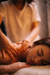 Professional female hands giving doing back massage to young brunette woman in spa salon with soft lighting, close-up. Concept of luxury professional massage. Concept of body care.