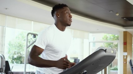 Wall Mural - From below fit African American man running on electric treadmill in gym on daytime. Sportsman working out on training machine.