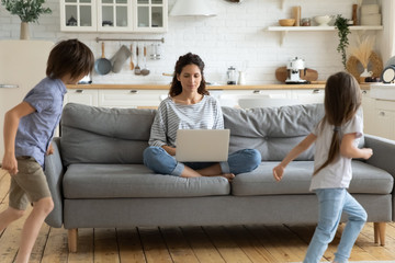 Calm young mother work on laptop sitting with children