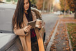 © klepach - Young pretty woman with cup of coffee and texting blog on tablet in autumn park near vehicle