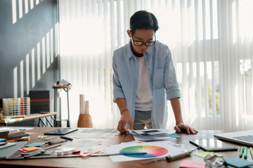 Wall Mural - working with inspiration. young asian man in eyeglasses analyzing new design project while standing 