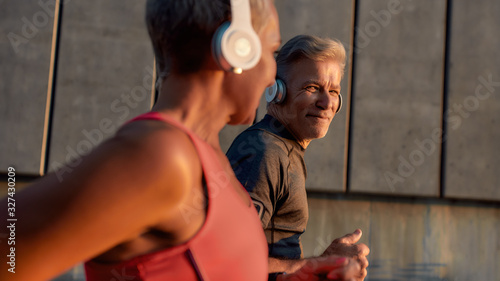 Ideal running partner. Portrait of happy and healthy middle-aged couple in headphones running together through the city street and smiling