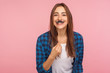 Portrait of cheerful playful girl in checkered shirt holding fake curled mustache on stick and smiling to camera, having fun, wearing masquerade accessory. studio shot isolated on pink background