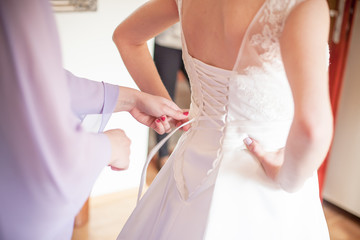 Wall Mural - Young bride getting ready for ceremony. Dressing up white wedding dress with ribbon bow. Preparation background.