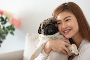 Wall Mural - Beautiful Asian young woman playing with her pet and smile with pug dog looking in funny face in bedroom