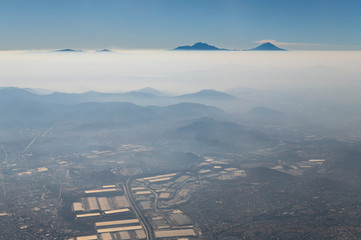 Aerial view of Mexico City in the smog and mist with the active Popocatepetl and dormant Iztaccihuatl volcano at the horizon, Mexico.