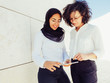 © Mangostar - Happy excited female employees watching content on tablet. Business women in office suits and hijab using tablet and looking at screen together. Digital technology in global business concept