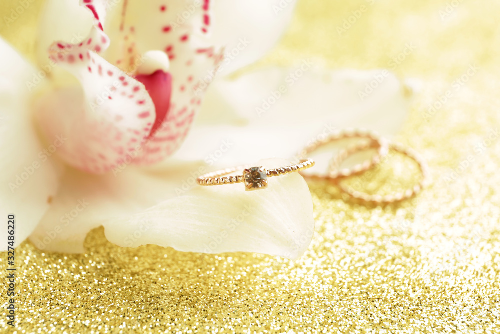 Flower with beautiful wedding and engagement rings on golden background