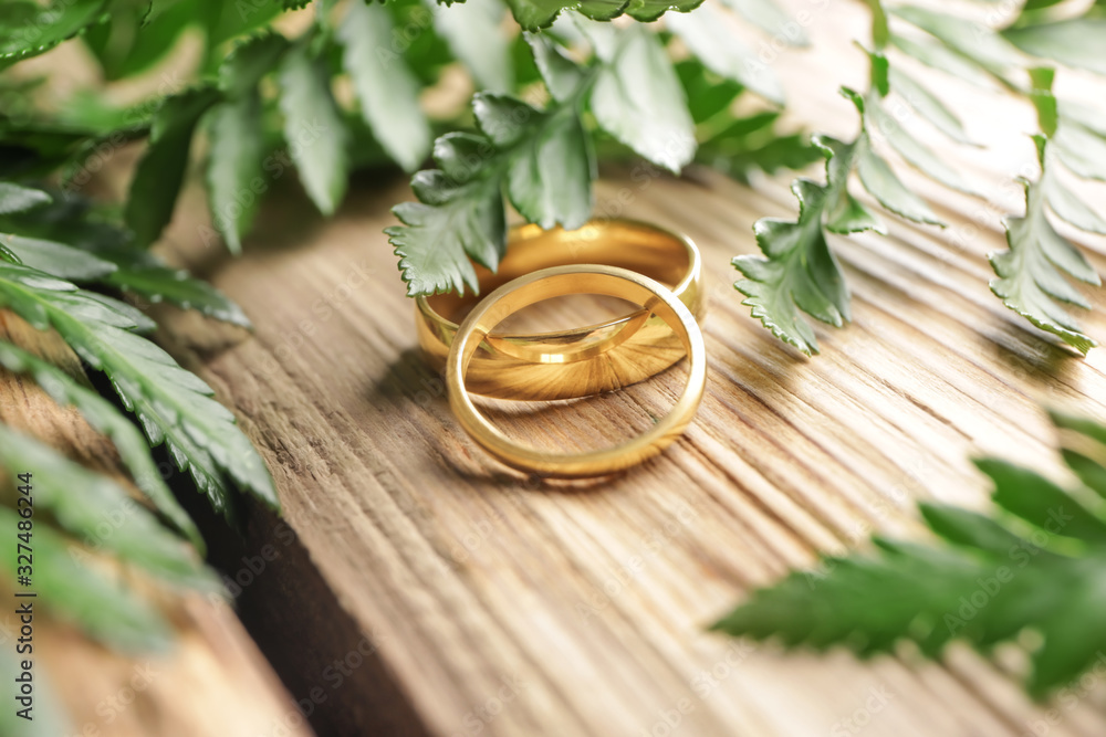 Leaves with beautiful wedding rings on wooden background
