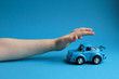 Blue toy car on a blue background and a children's hand that wants to take it