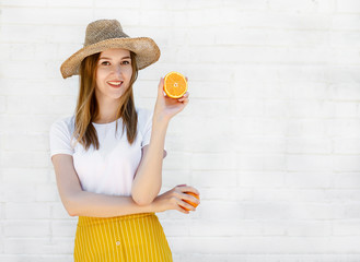 Portrait of a cheerful young girl in Hat holding two slices of orange on white wall background