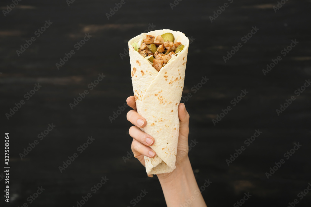 Female hand with tasty doner kebab on dark background