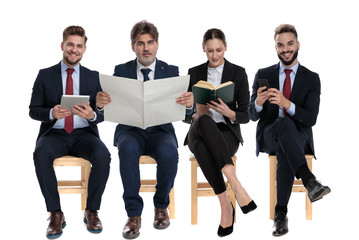 Poster - 4 businessmen reading from book, newspaper, phone and tablet