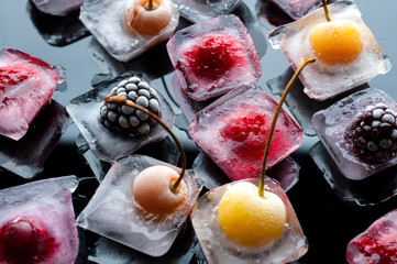  frozen raspberries berries cherries and blackberries in pieces of ice in a glass bowl on a black background