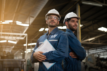 Wall Mural - Portrait of two factory technicians. They folded and took pictures in a factory with the golden light of the sun.  They wear uniforms, safety helmets, and protective goggles.