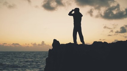 Wall Mural - A man in a jacket stands on a rock by the sea in a stormy weather at dawn	