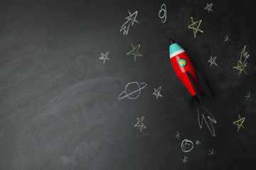 bright toy rocket and drawings on chalkboard, flat lay. space for text