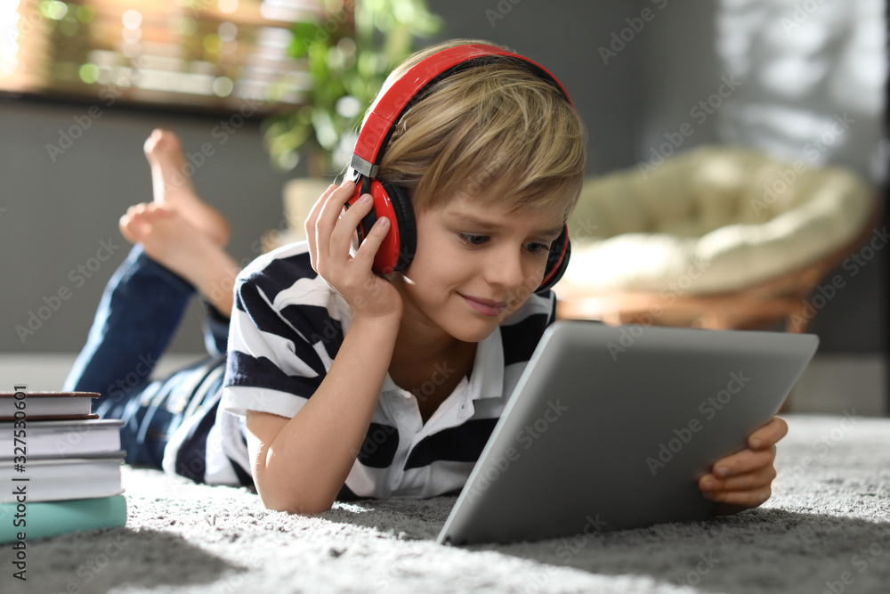 Cute little boy with headphones and tablet listening to audiobook at home - obrazy, fototapety, plakaty 