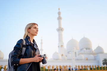 Traveling by Unated Arabic Emirates. Pretty Young Woman with camera standing near the Sheikh Zayed Grand Mosque, famous Abu Dhabi sightseeing.