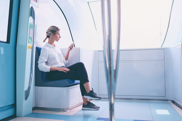 Wall Mural - Enjoying travel. Young pretty woman traveling by the metro train sitting near the window using smartphone.