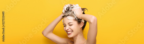 Fotografía panoramic shot of happy girl with closed eyes washing hair on yellow background
