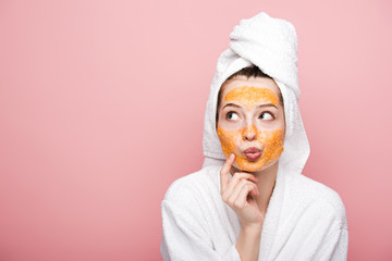 pensive girl with citrus facial mask touching face while looking away isolated on pink