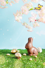 Easter Colored Eggs, Chocolate Easter Bunny And Blooming Spring Tree Branches Over Blue Background.