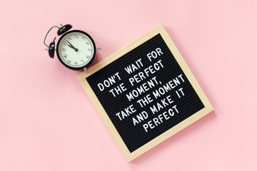 Wall Mural - Don't wait for the perfect moment, take the moment and make it perfect. Motivational quote on letter board, black alarm clock on pink background. Concept inspirational quote of the day