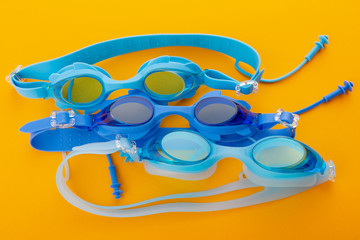 Wall Mural - three blue swimming goggles lie on a yellow background, concept, close-up