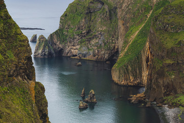 Amazing rocky coastline of Vestmannaeyjar island in Iceland. High green rocky mountains and ocean bay. Nature background.