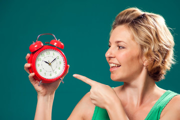 A portrait of smiling woman holding alarm clock and point at it. People and emotions concept