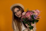 Fototapeta Tulipany - Laughing girl in glasses holding eustoma bouquet isolated on yellow background