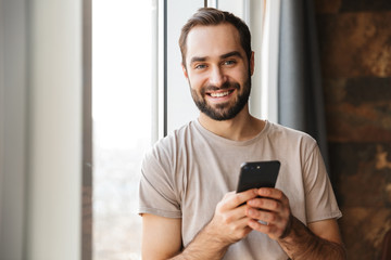 Wall Mural - Cheery young man indoors chatting by mobile phone.