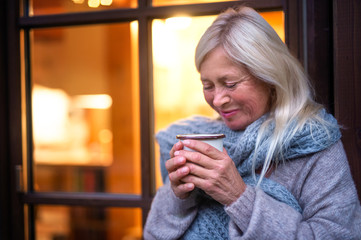 Wall Mural - Senior woman with coffee standing outdoors on terrace, resting.