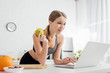 © LIGHTFIELD STUDIOS - selective focus of sportive woman holding tasty apple and using laptop