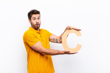 Wall Mural - young handsome man surprised, shocked, amazed, holding the letter C of the alphabet to form a word or a sentence.