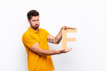 Wall Mural - young handsome man angry, anger, disagreement, holding the letter F of the alphabet to form a word or a sentence.