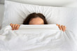 © cunaplus - Top view shot of a young woman hiding face under blanket while lying in cozy bed.