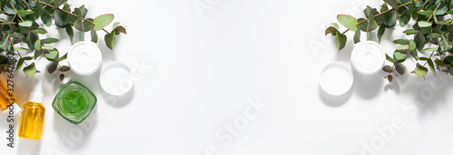Fotografía Long wide banner with natural herbal cosmetic creams, scrubs and oils and fresh eucalyptus leaves on white background
