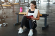 © Prostock-studio - Attractive woman with notebook planning her workout schedule in sports club