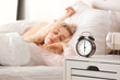 © Pixel-Shot - Alarm clock on table of sleeping young woman in bedroom