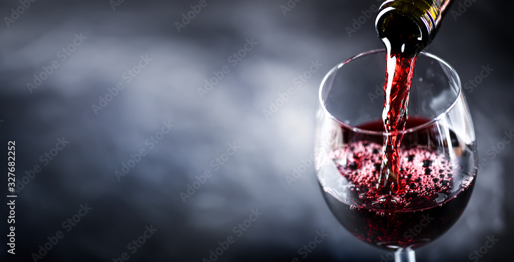 Pouring glass of red wine from a bottle in wide banner shape or copy space for text.. - obrazy, fototapety, plakaty 