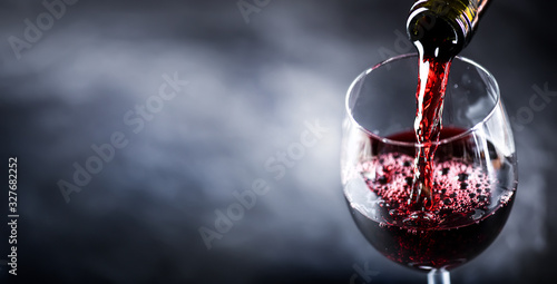 Pouring glass of red wine from a bottle in wide banner shape or copy space for text.. © Milan