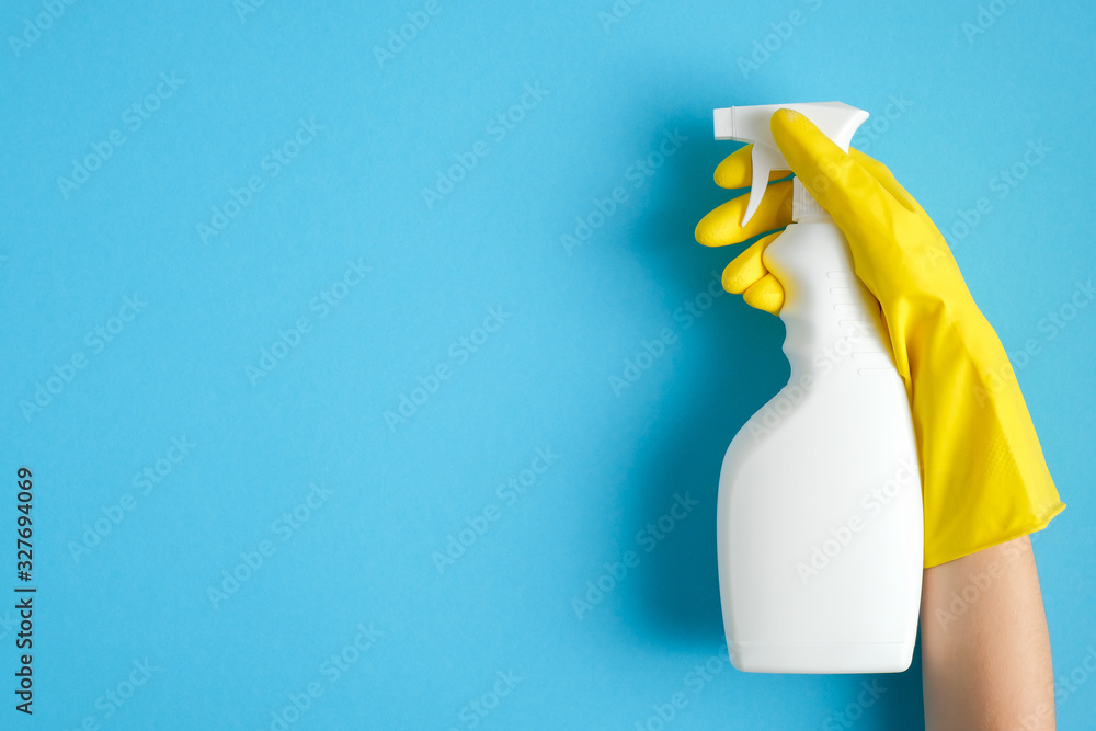 Hand in a yellow rubber glove holds cleaner spray bottle over blue background. Cleaning service banner mockup. Housecleaning and housekeeping concept. Flat lay, top view - obrazy, fototapety, plakaty 