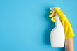 Hand in a yellow rubber glove holds cleaner spray bottle over blue background. Cleaning service banner mockup. Housecleaning and housekeeping concept. Flat lay, top view